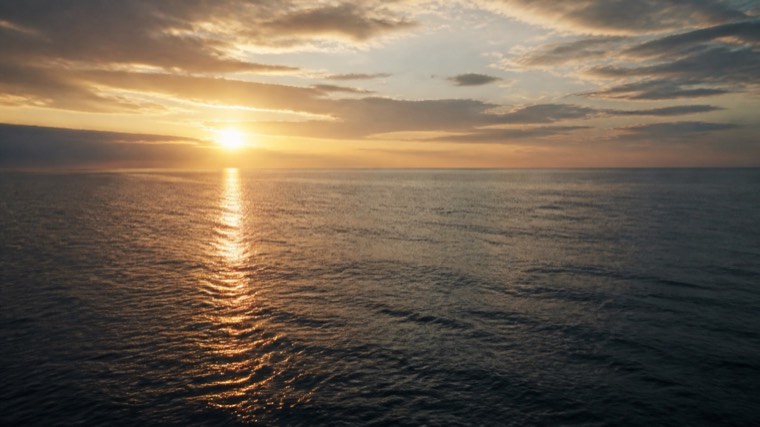 Aerial still: open ocean with the sun low on the horizon