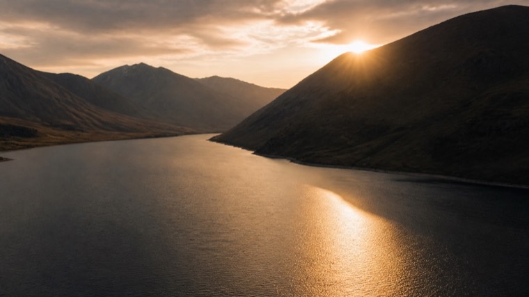 Aerial still: a mountain lake with the sun behind the ridge